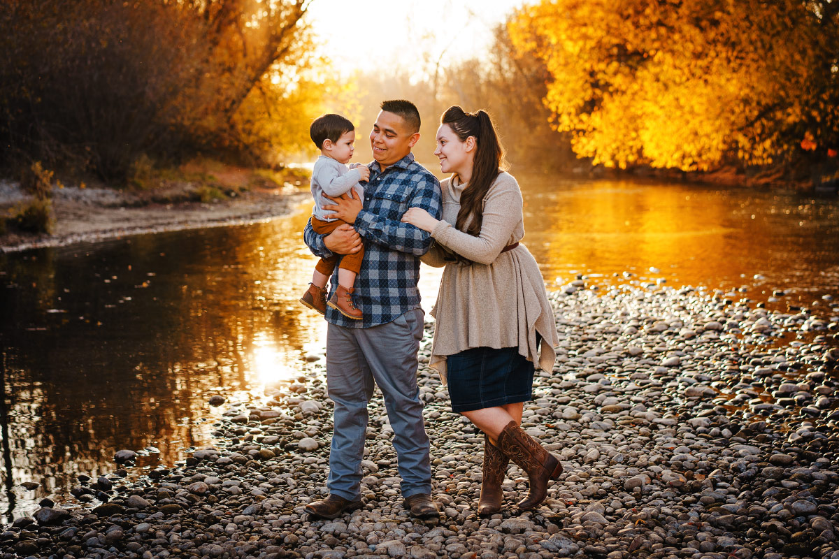 Young family stands on banks of Boise River in late fall
