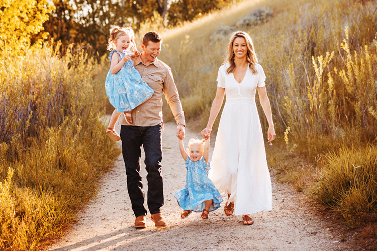 Young family walks hand in hand down gravel path at Boise's Military Reserve Park on photoshoot