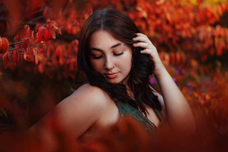 Senior photo of teen girl framed by vibrant red plants for autumn photoshoot
