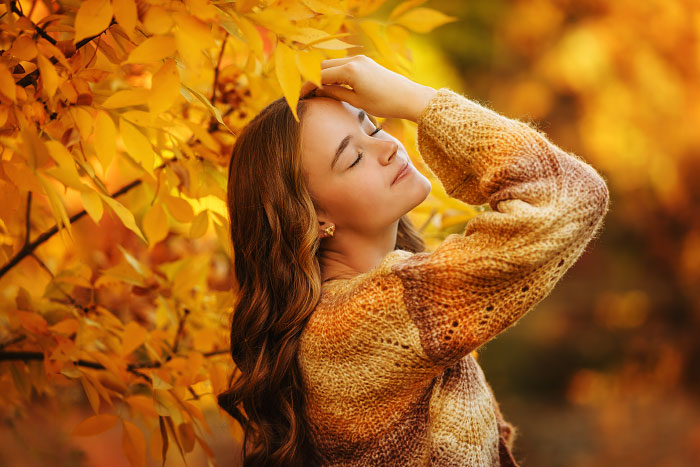 Young woman with eyes closed poses against golden tree for fall senior photos at Kathryn Albertson Park, Boise, Idaho