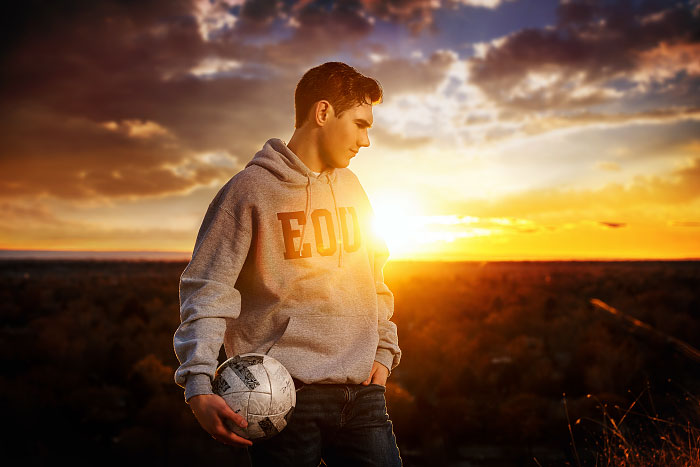 High school boy holds soccer ball under one arm at sunset at Camel's Back Park in Boise