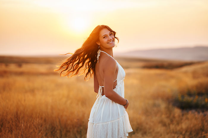 Teen girl in white dress flips hair at sunset for senior photo session