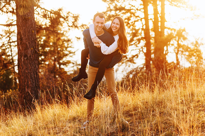 Young man giving young woman a piggyback ride for engagement session outside Boise Idaho