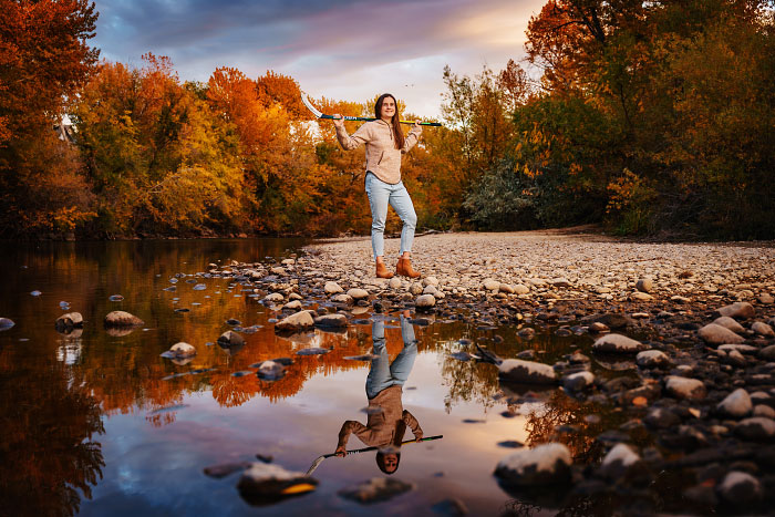 Senior girl holding hockey stick above shoulders reflected in Boise River, Idaho
