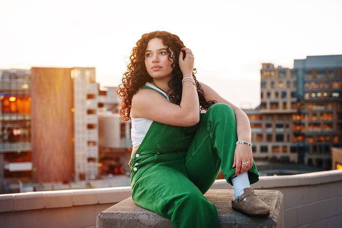 Curly-haired girl sitting on parking garage rooftop at sunset in downtown Boise