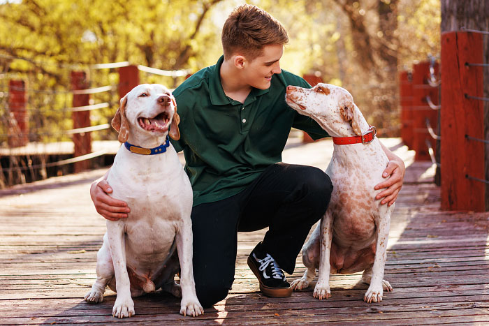 High school boy kneeling between two dogs on dock by Boise River