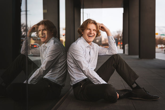 High school boy sits with back to mirrored wall in downtown city