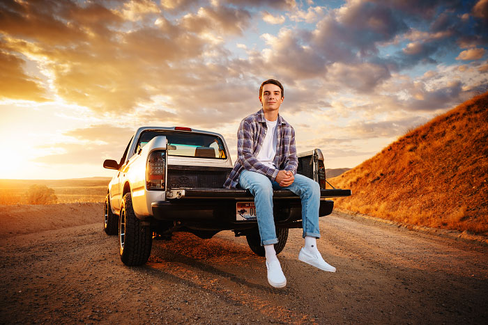 Senior boy sits on back of pickup truck at sunset for high school senior session in Eagle foothills of Idaho