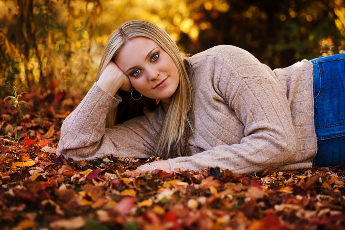 Blonde girl in sweater lying in leaves for senior photo session