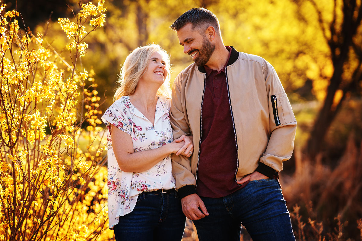 Woman gazes lovingly into man's eyes by golden forsythia plant in springtime at Boise's Kathryn Albertson Park