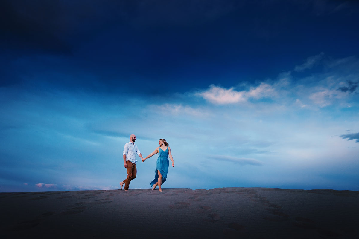 Young couple walk hand in hand across sand dune at twilight at Idaho's Bruneau Dunes State Park