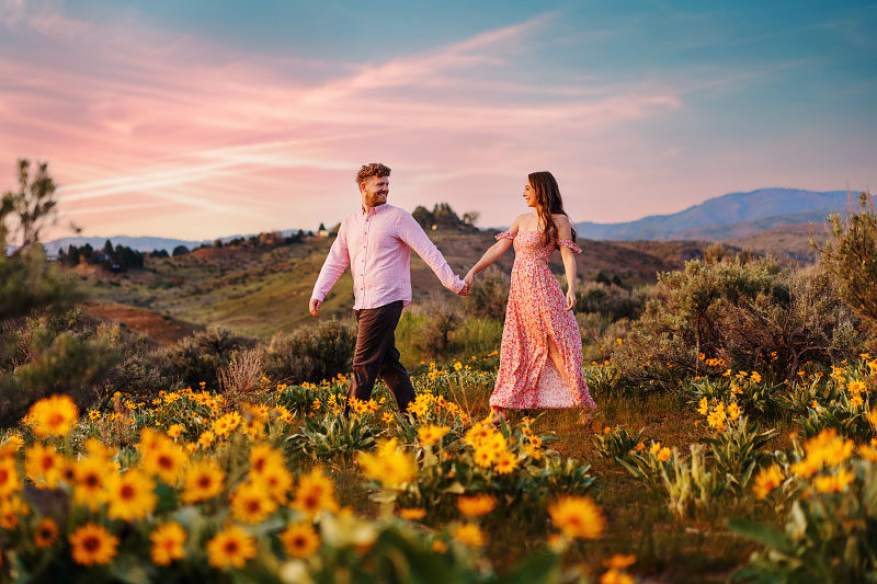 Young couple walking through field of yellow flowers in hills outside Boise in springtime
