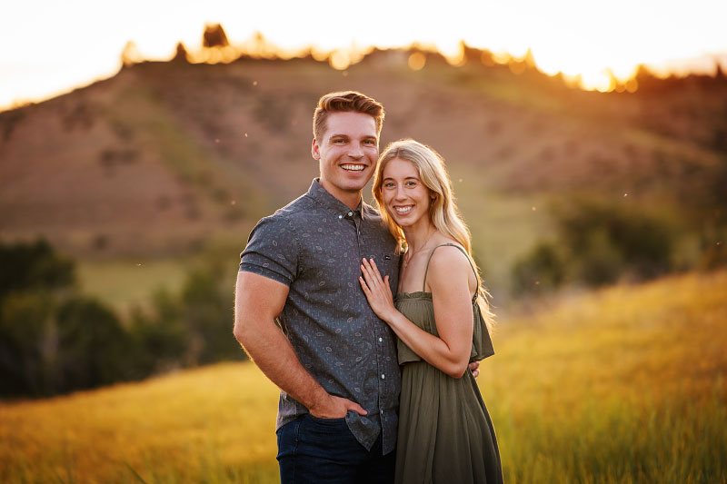 Young couple looks at camera at sunset for engagement photoshoot