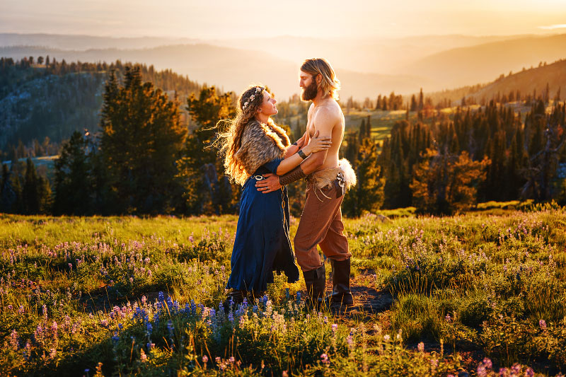 Young couple dressed in viking attire embrace atop mountain meadow in Idaho at sunset