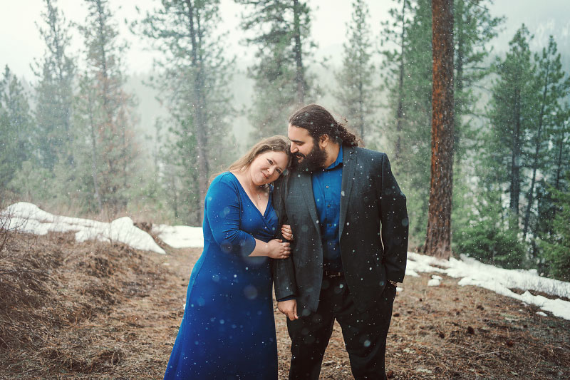 Young couple in Idaho woods surrounded by snow showers