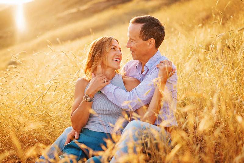 Couple sitting in golden field gazing into each others' eyes at sunset in Boise foothills