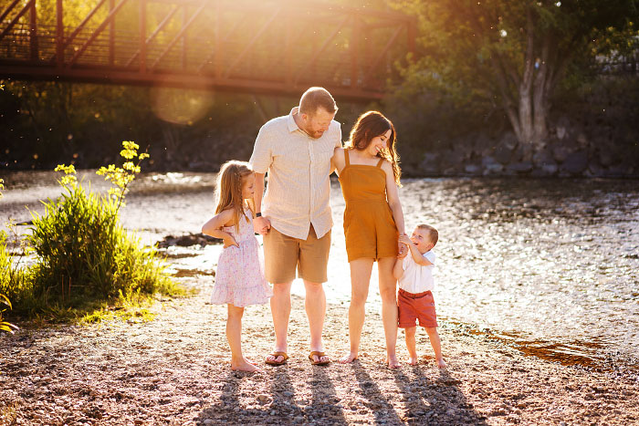 Young family holds hands by Boise River in Eagle, Idaho