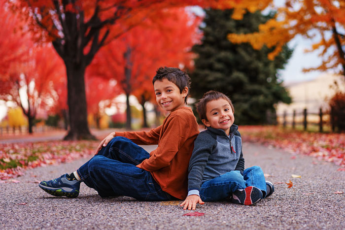 Two young boys sit back to back under red maple trees for fall family photos in southeast Boise