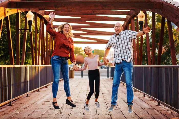 Mom, Dad, and elementary school daughter jump in unison on bridge in Indian Creek Plaza, Caldwell, Idaho