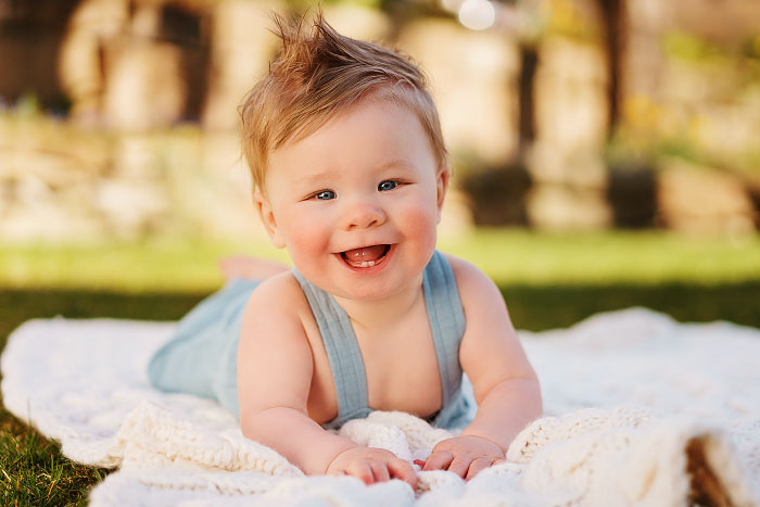Smiling baby with mohawk lies on blanket for photoshoot in Boise