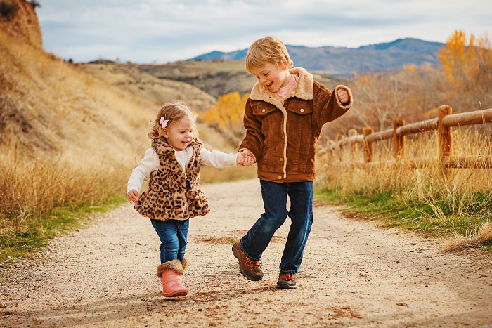 Two small children skip down path holding hands at Military Reserve Park in Boise