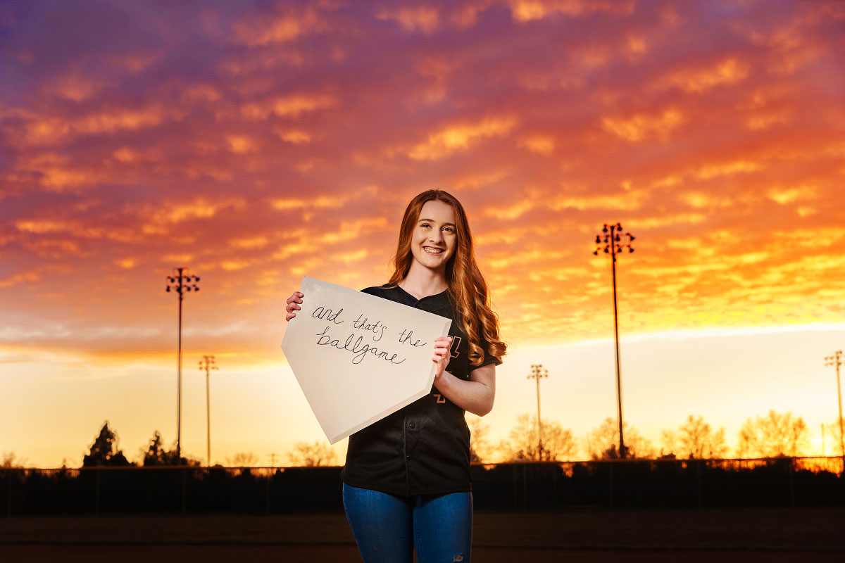 Teen girl holding home plate on baseball field for senior session in Boise