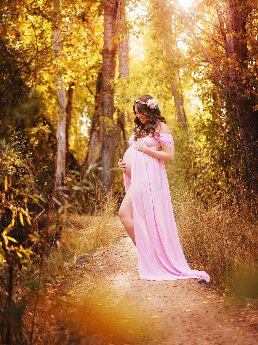 Young pregnant woman in pink gown and flower grown posing on dirt path in Boise foothills for maternity photos