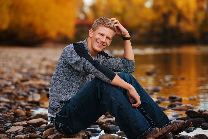 High school senior picture of senior boy sitting by Boise River in autumn