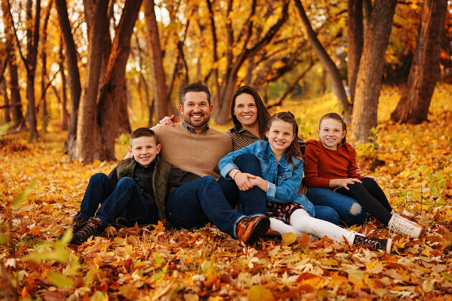 Family of five sitting on carpet of autumn leaves by Eagle River Greenbelt outside Boise Idaho